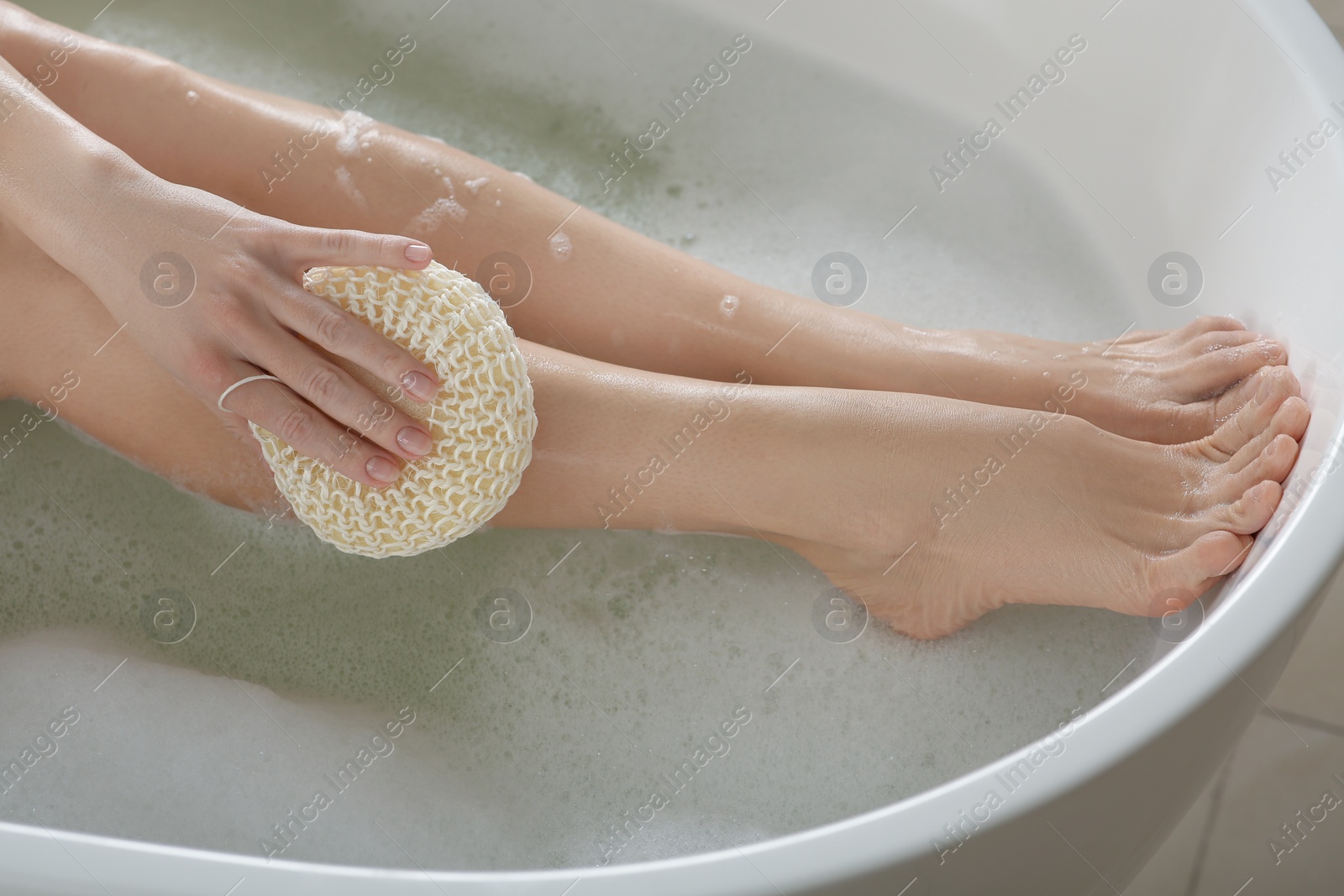 Photo of Woman rubbing her leg with sponge while taking bath, closeup