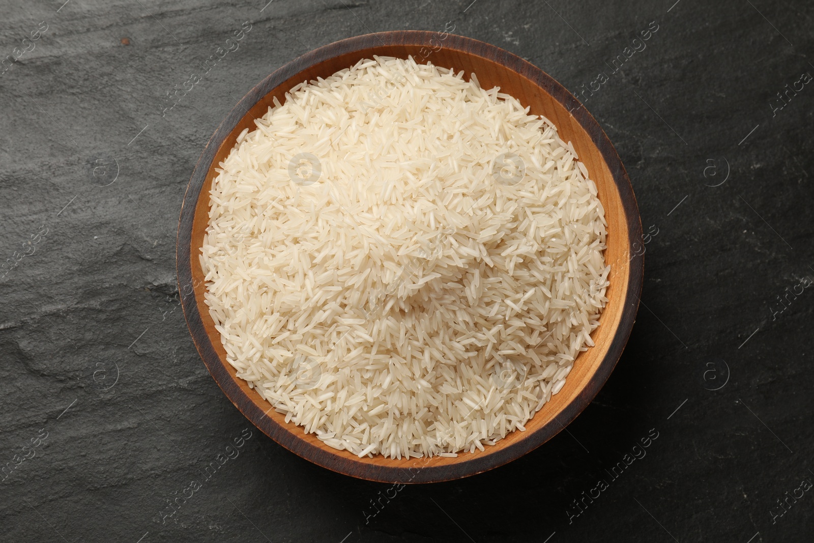 Photo of Raw basmati rice in bowl on black table, top view