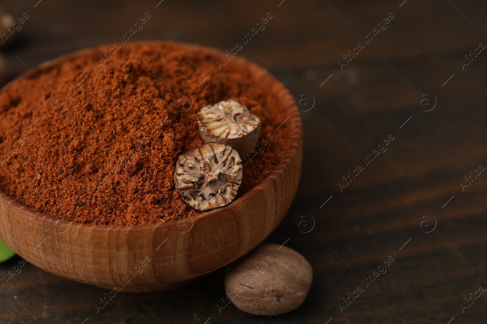Photo of Nutmeg powder and halves of seed in bowl on wooden table, closeup. Space for text