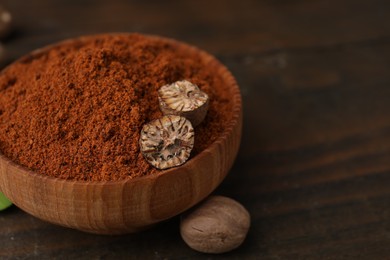 Nutmeg powder and halves of seed in bowl on wooden table, closeup. Space for text