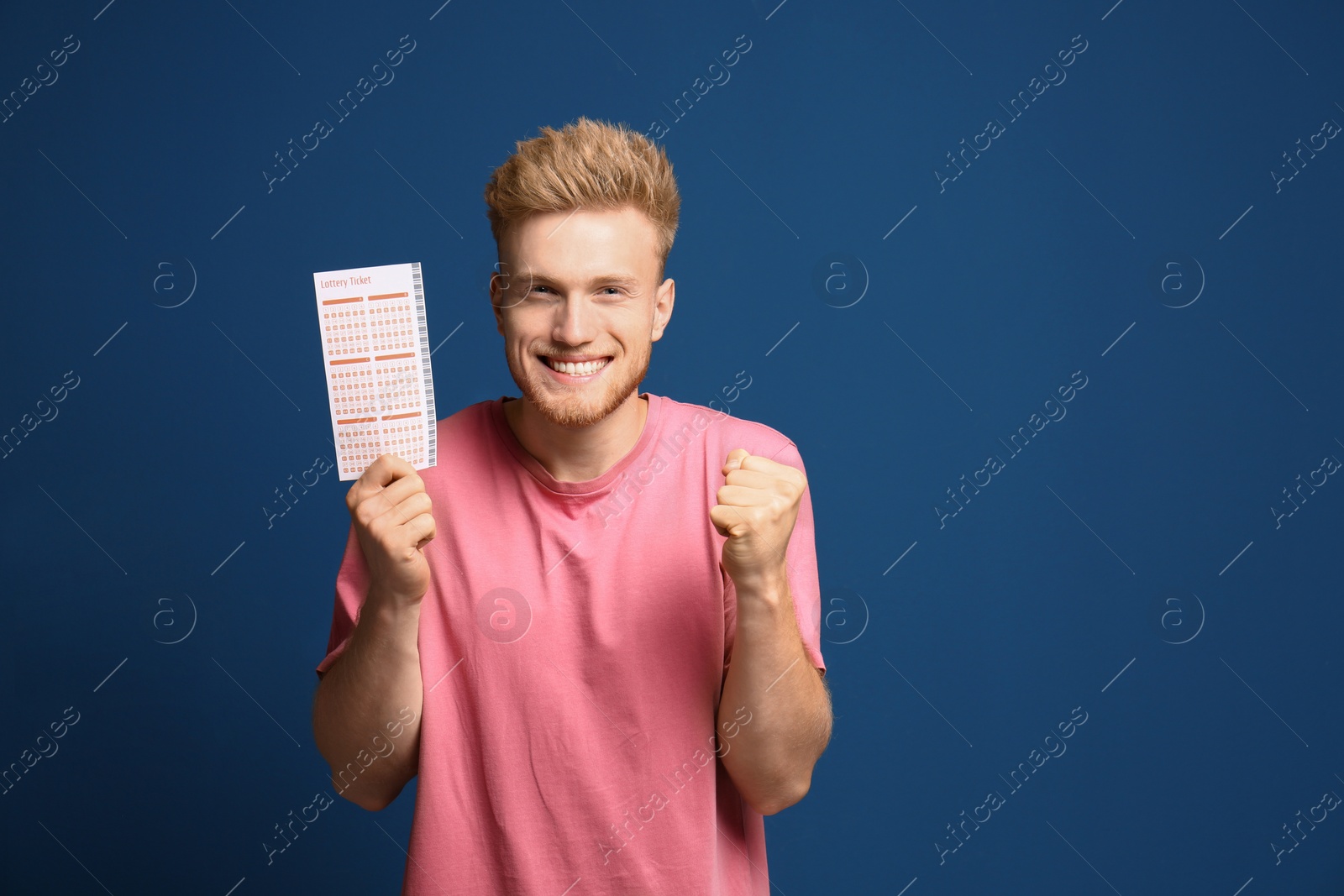 Photo of Portrait of happy young man with lottery ticket on blue background