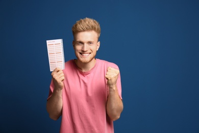 Photo of Portrait of happy young man with lottery ticket on blue background