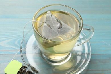 Tea bag in cup with hot drink and dry leaves on light blue wooden table, closeup