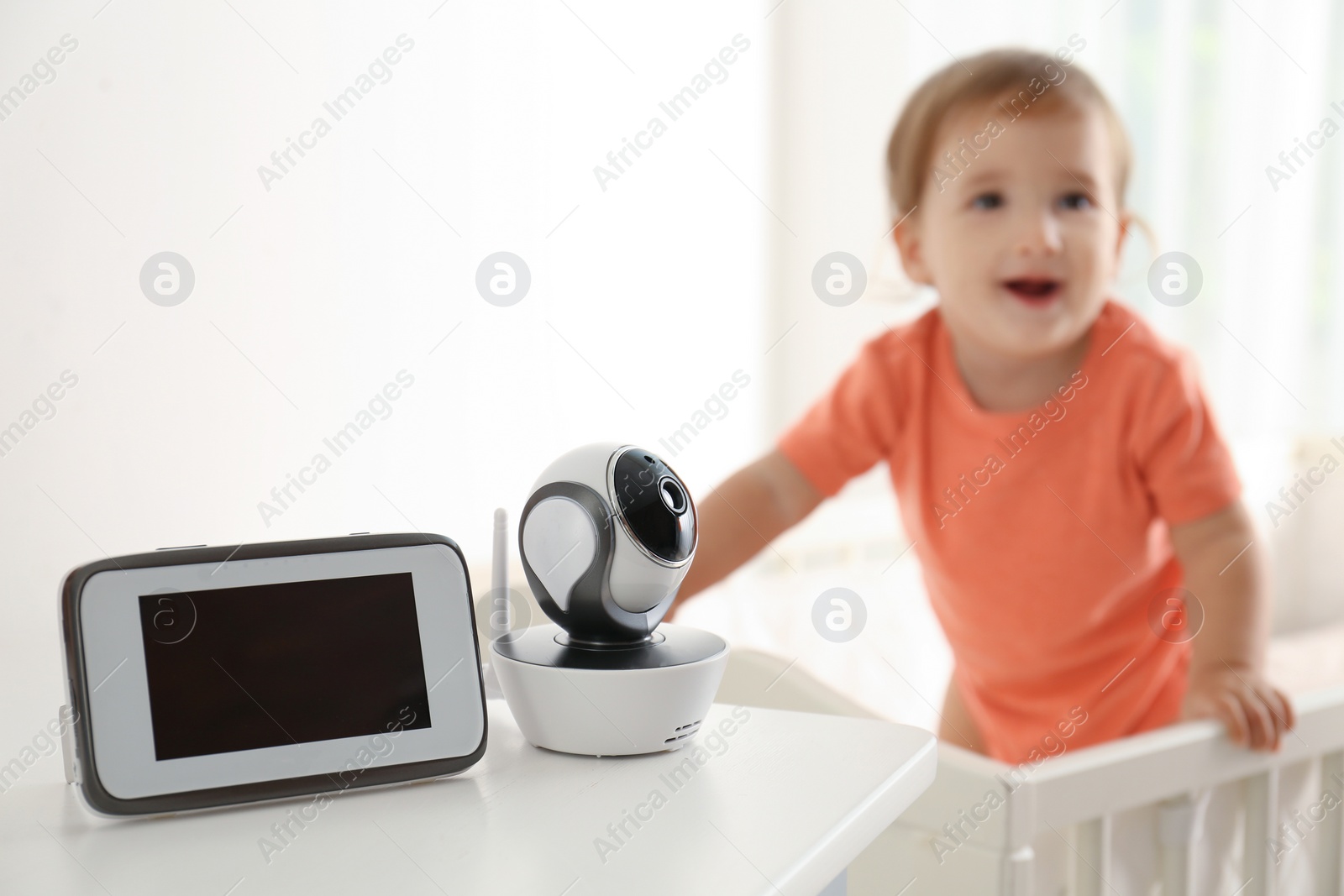 Photo of Baby monitor and camera on table near crib with child in room. Video nanny