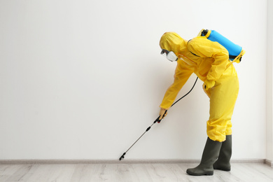 Pest control worker in protective suit spraying pesticide indoors. Space for text