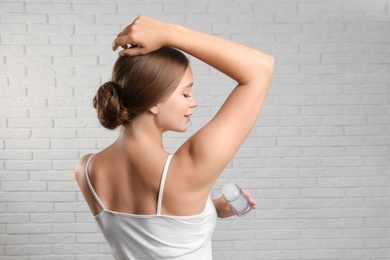 Photo of Young woman applying crystal alum deodorant to armpit against brick wall