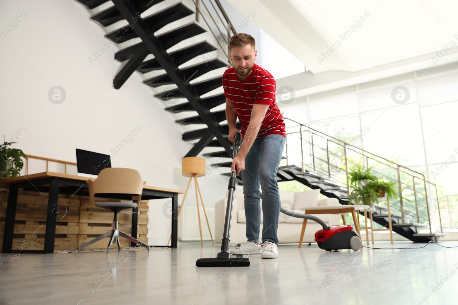 Photo of Young man using vacuum cleaner in living room