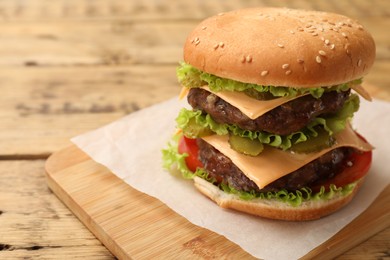 Photo of Tasty hamburger with patties on wooden table, closeup. Space for text