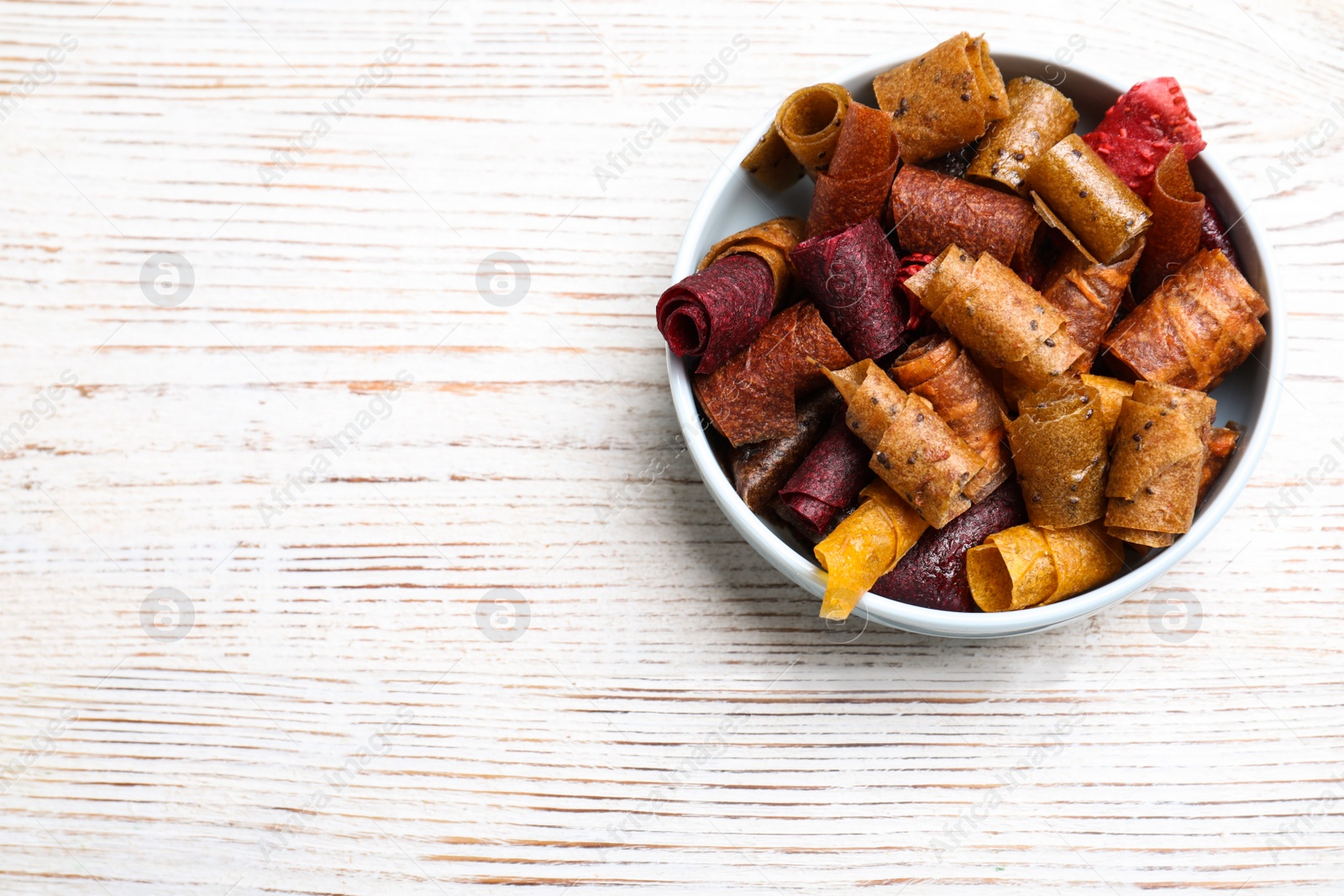 Photo of Delicious fruit leather rolls on white wooden table, top view. Space for text