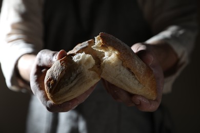 Man breaking loaf of fresh bread on dark background, closeup