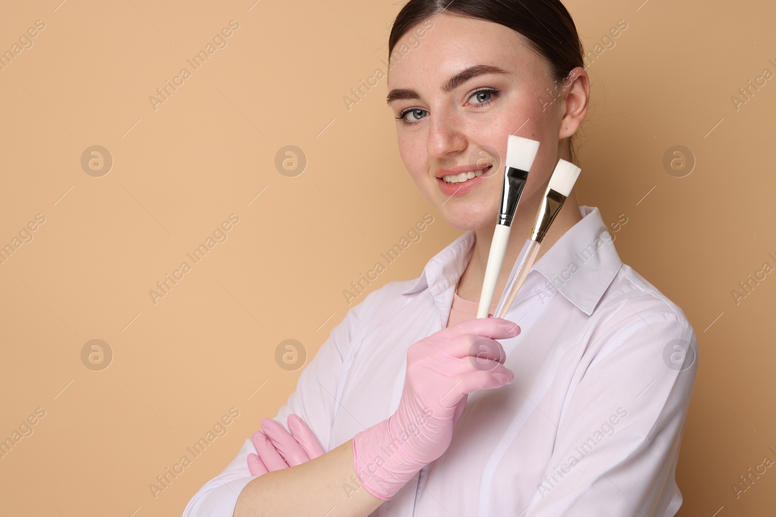 Photo of Cosmetologist with cosmetic brushes on beige background, space for text