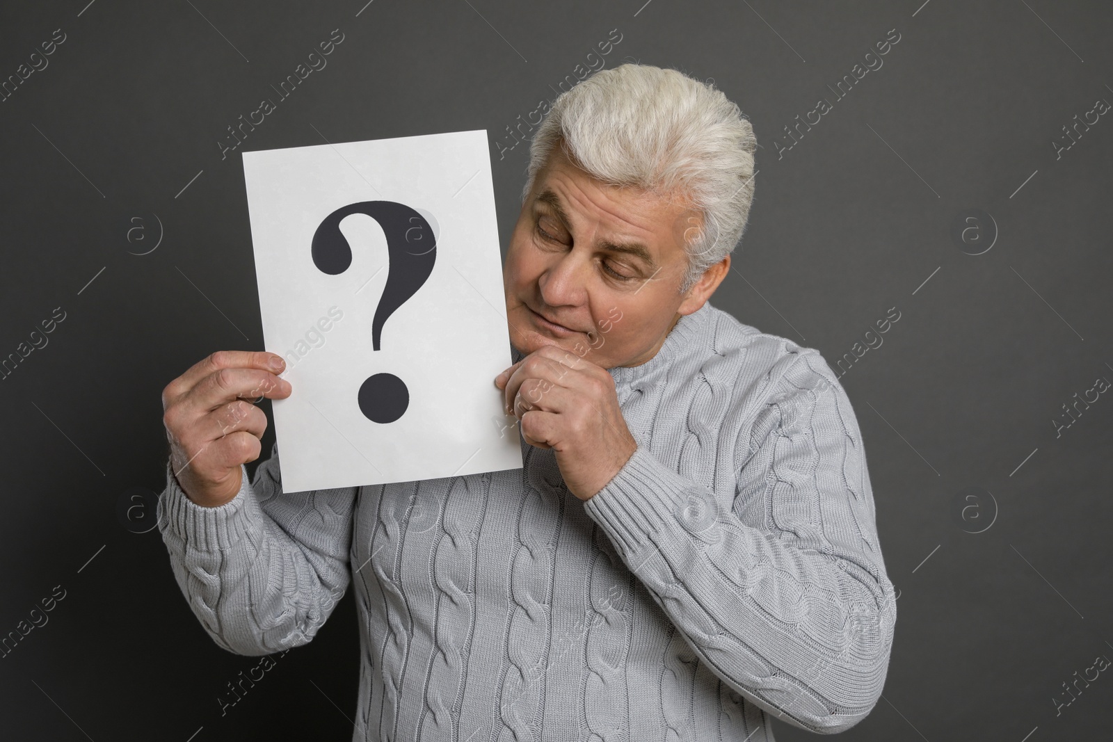 Photo of Emotional mature man holding paper with question mark on dark grey background