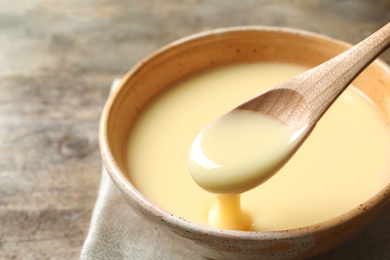 Spoon of pouring condensed milk over bowl on table, closeup with space for text. Dairy products