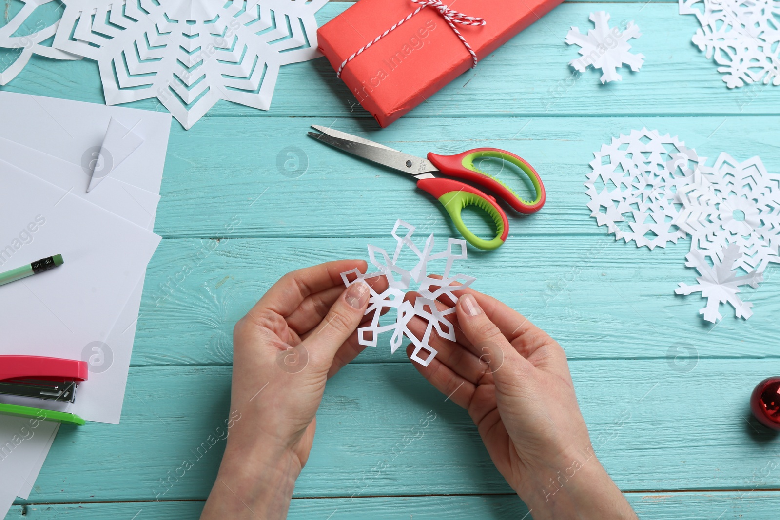 Photo of Woman making paper snowflake at turquoise wooden table, top view
