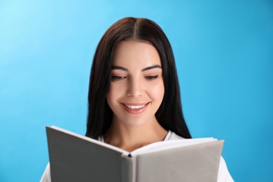 Photo of Beautiful young woman reading book on light blue background