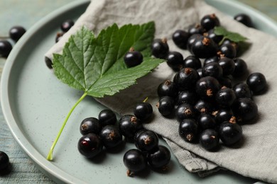 Photo of Ripe blackcurrants, leaves, napkin and plate on table, closeup