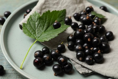 Ripe blackcurrants, leaves, napkin and plate on table, closeup