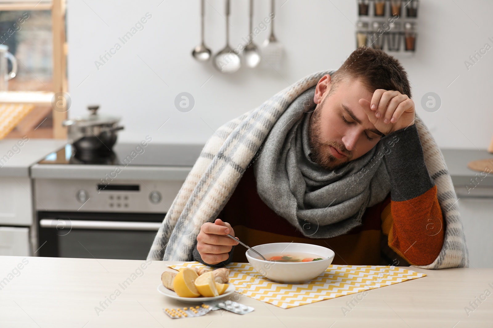 Photo of Sick young man eating tasty soup to cure flu at table in kitchen