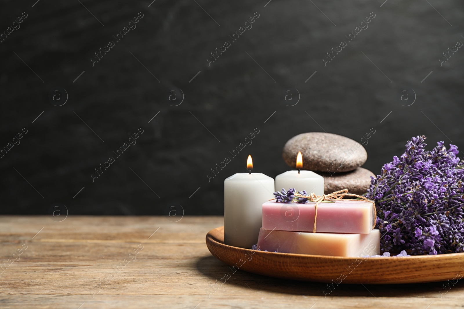 Photo of Burning candles, stones, soap bars and lavender flowers on wooden table. Space for text