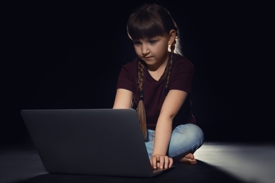 Photo of Little child using laptop on dark background. Cyber danger