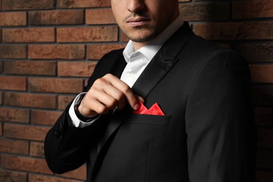 Photo of Man fixing handkerchief in breast pocket of his suit near brick wall, closeup