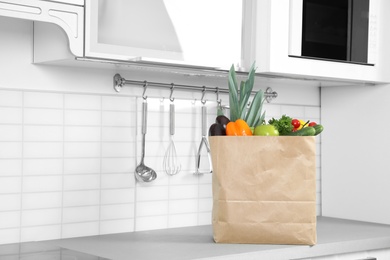 Photo of Paper shopping bag full of vegetables on countertop in kitchen. Space for text