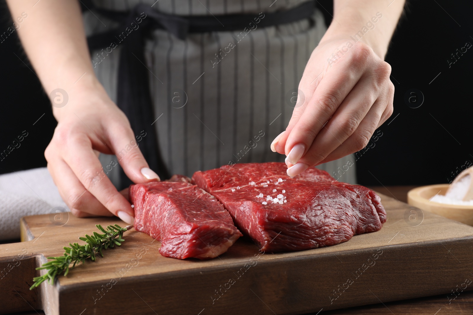 Photo of Woman salting fresh raw beef steak at table, closeup