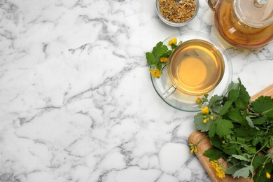 Photo of Aromatic celandine tea and flowers on white marble table, flat lay. Space for text