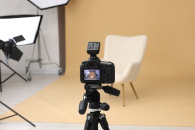 Photo of Camera on tripod, armchair and professional lighting equipment in modern photo studio