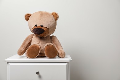 Cute teddy bear on cabinet near light wall, space for text