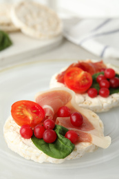 Photo of Puffed rice cakes with prosciutto, berries and basil on plate, closeup