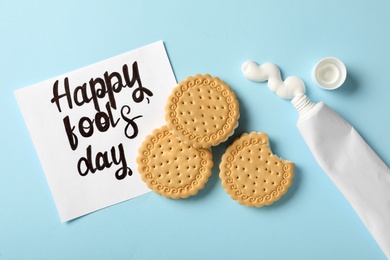 Cookies with toothpaste and Happy Fools' Day note on light blue background, flat lay