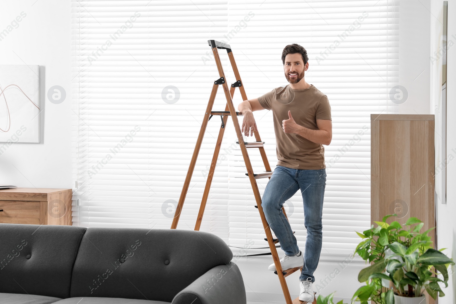 Photo of Man showing thumb up on wooden ladder at home