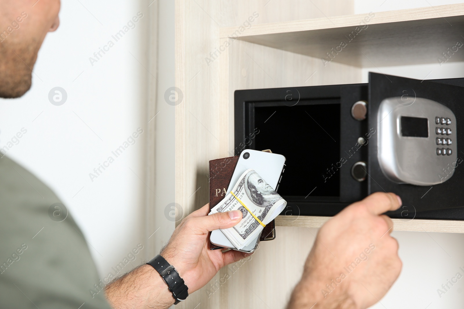 Photo of Man putting smartphone, passport and money into steel safe, closeup