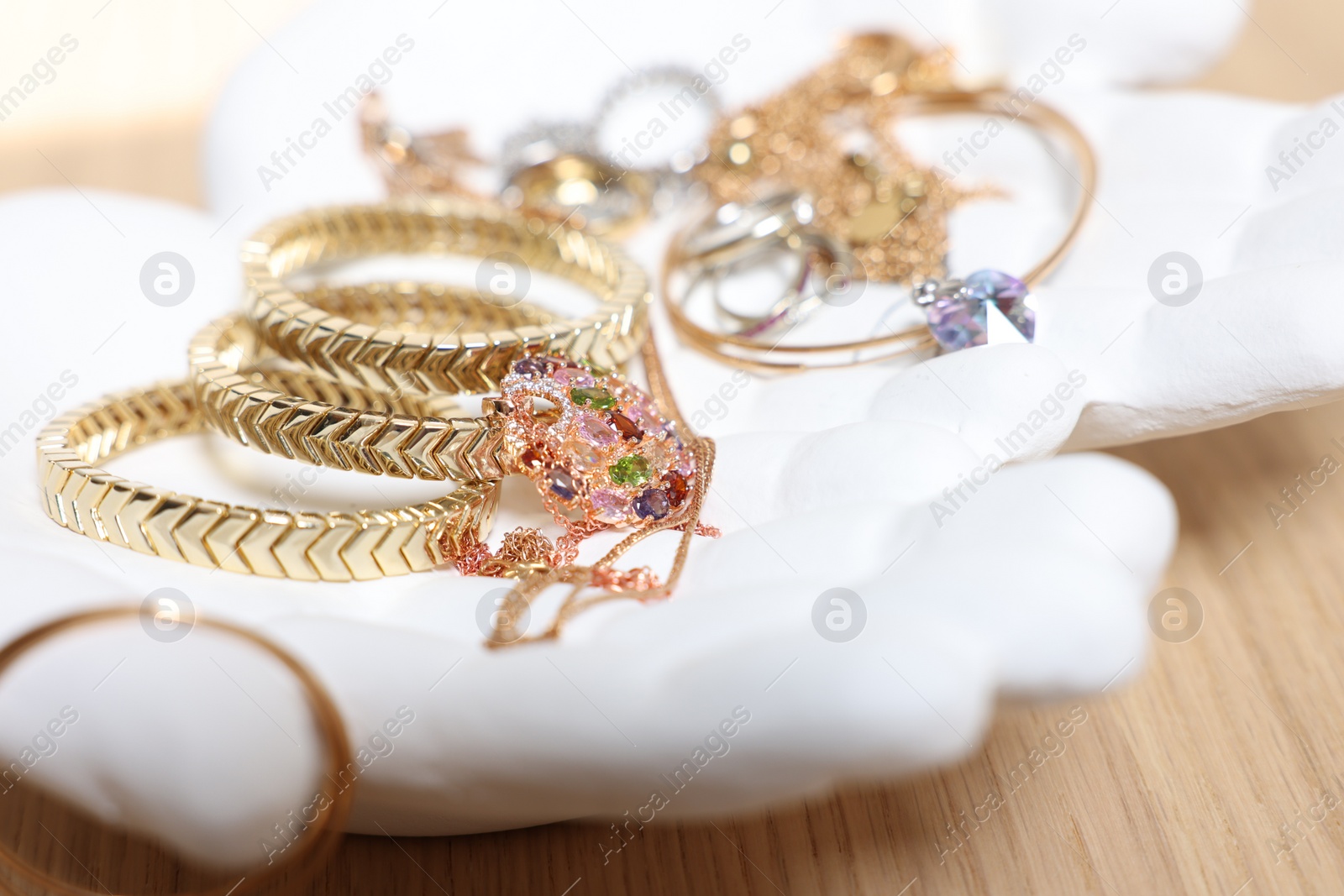 Photo of Ceramic hand stand with stylish bracelets and other accessories on wooden table, closeup