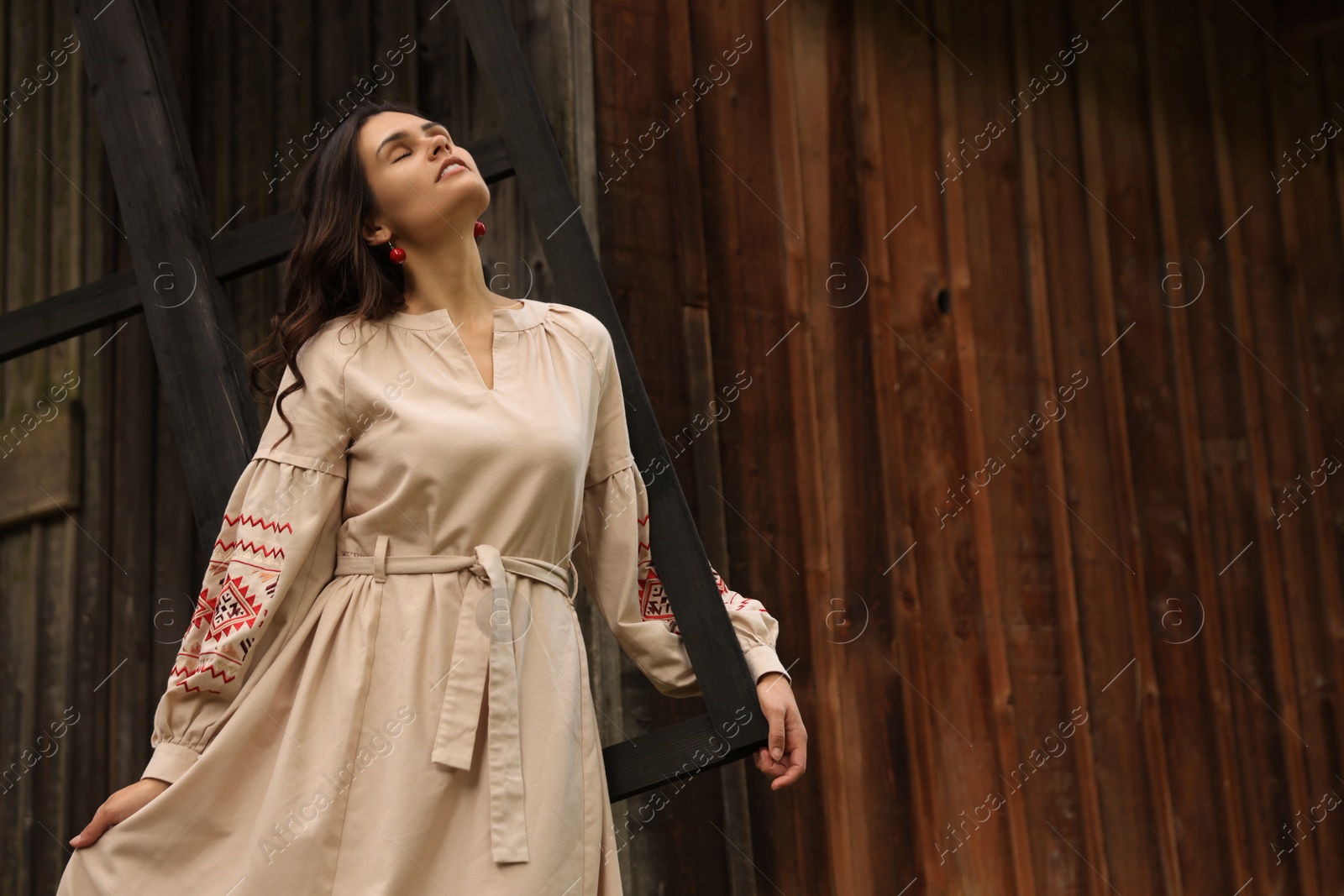 Photo of Beautiful woman wearing embroidered dress near old wooden mill in countryside. Ukrainian national clothes