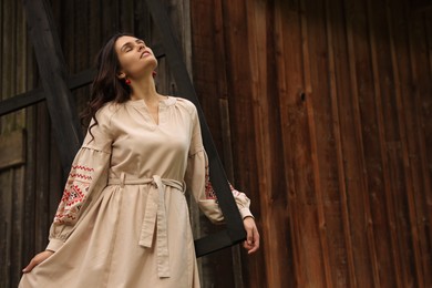 Photo of Beautiful woman wearing embroidered dress near old wooden mill in countryside. Ukrainian national clothes