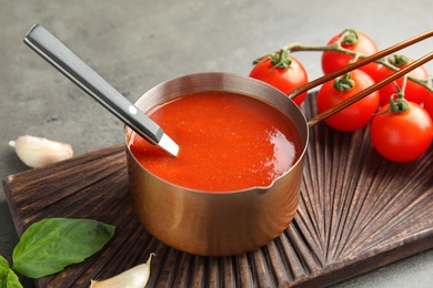 Pan with tomato sauce and spoon on wooden board, closeup