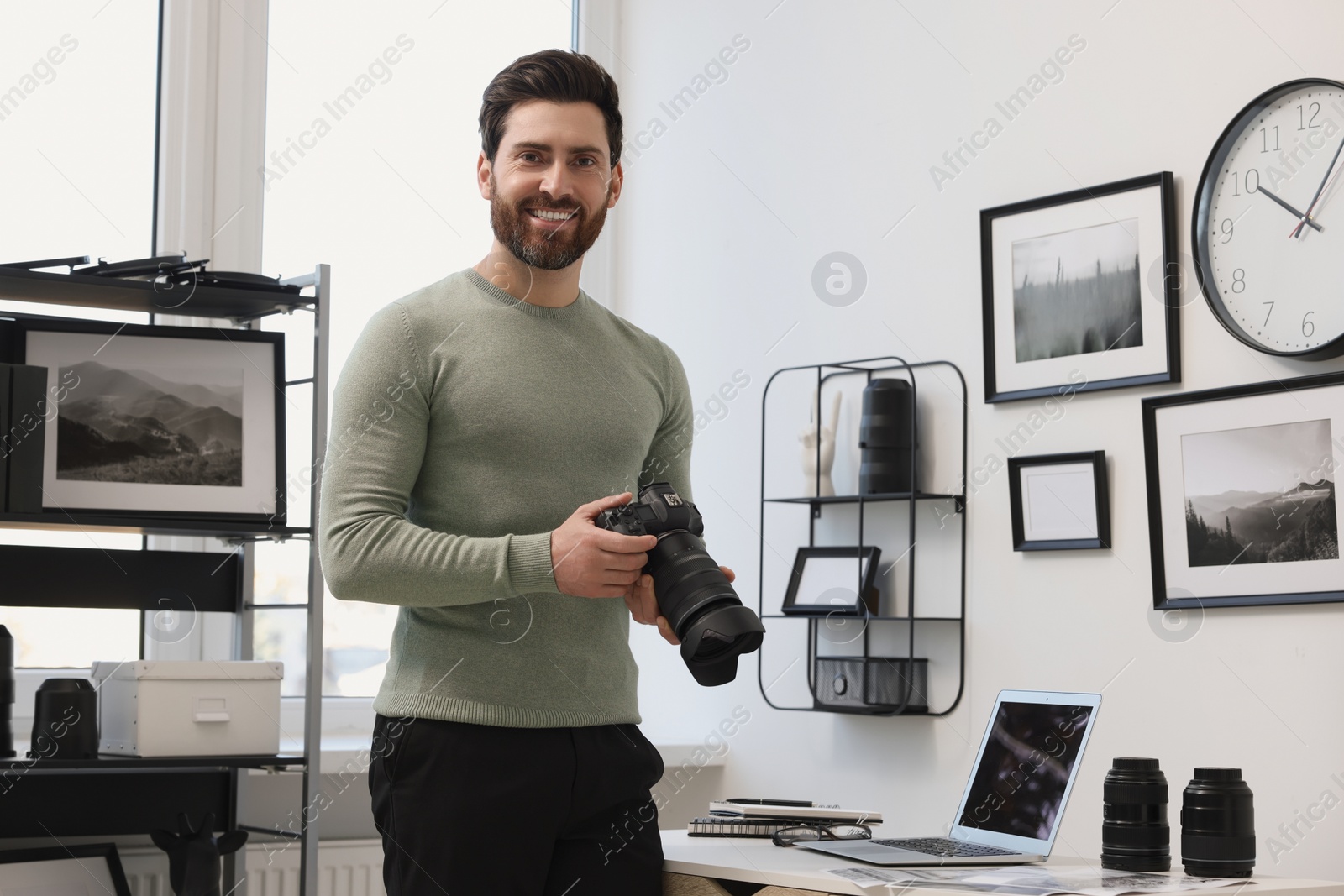 Photo of Professional photographer holding digital camera near table with laptop in office
