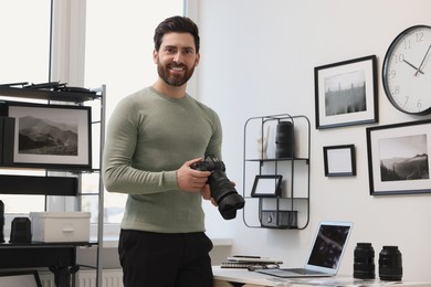 Professional photographer holding digital camera near table with laptop in office