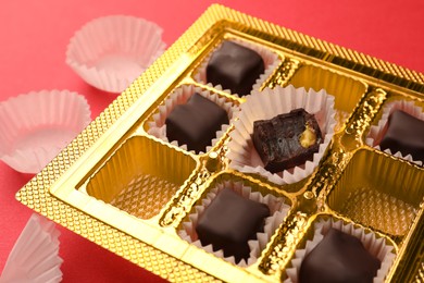 Photo of Partially empty box of chocolate candies on red background, closeup