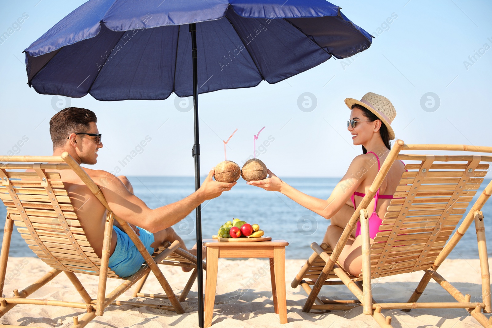 Photo of Couple with drinks resting on sunny beach at resort