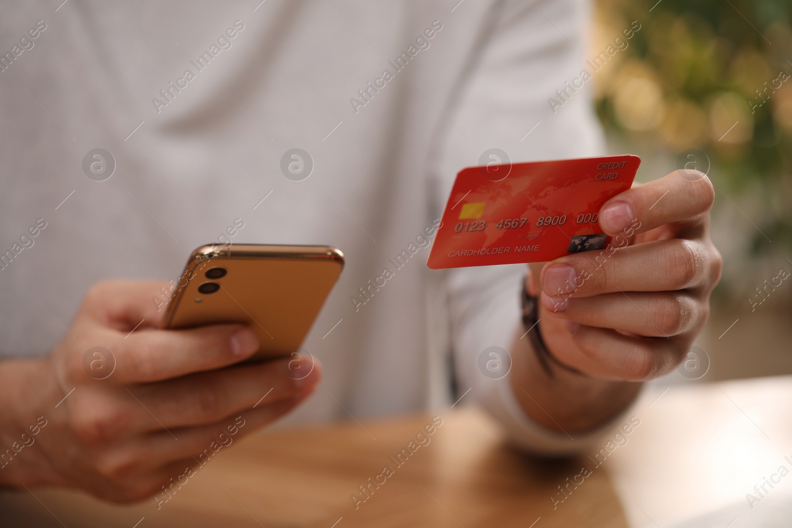 Photo of Man using smartphone and credit card for online payment at desk indoors, closeup