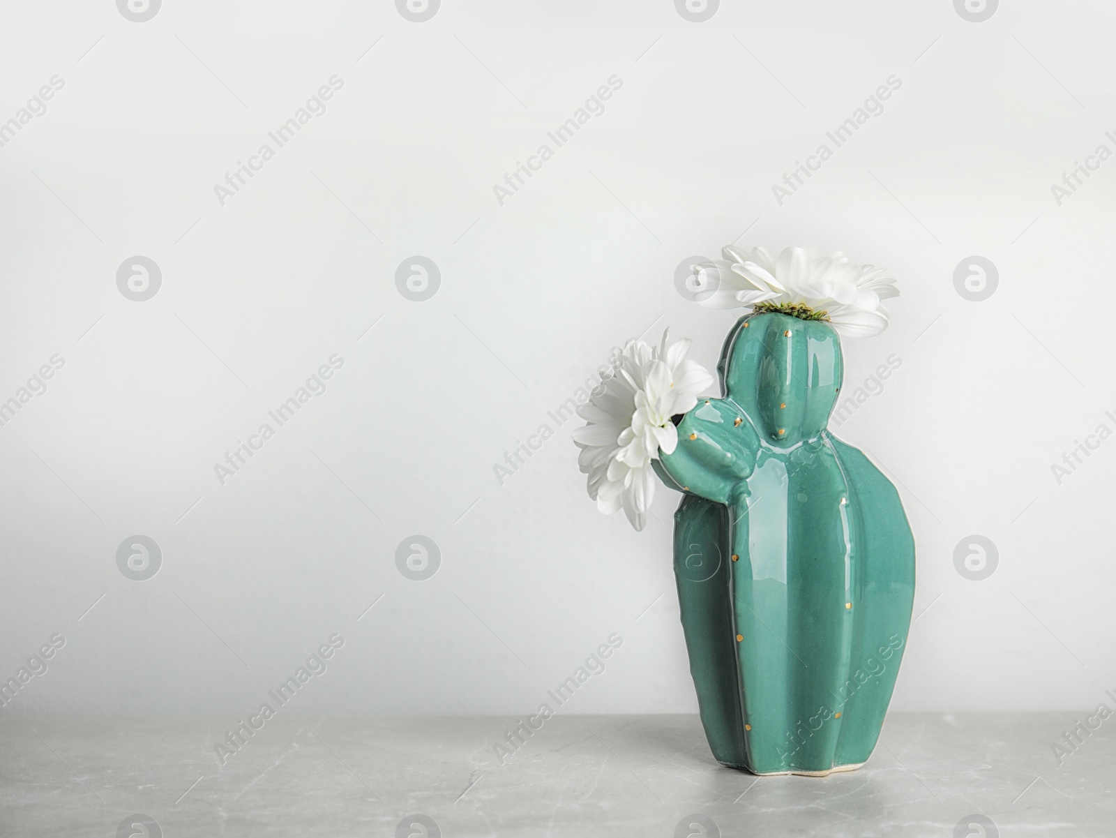 Photo of Trendy cactus shaped vase with flowers on table against light wall. Creative decor