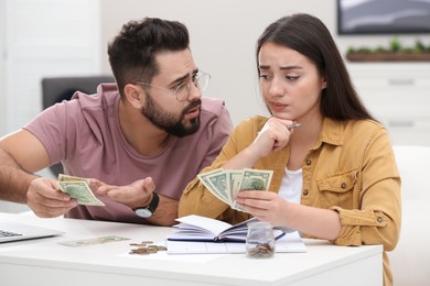 Photo of Worried young couple counting money at white table indoors