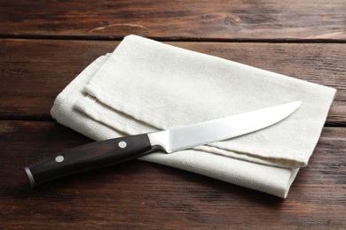 Photo of One sharp knife and napkin on wooden table, closeup