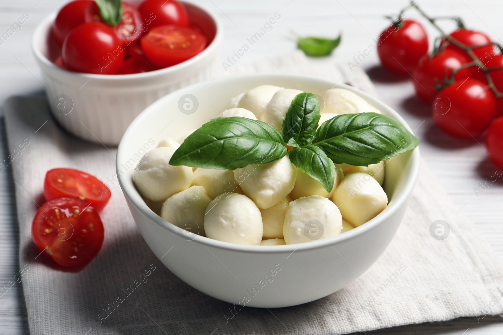 Photo of Delicious mozzarella balls, tomatoes and basil leaves in bowl on table, closeup