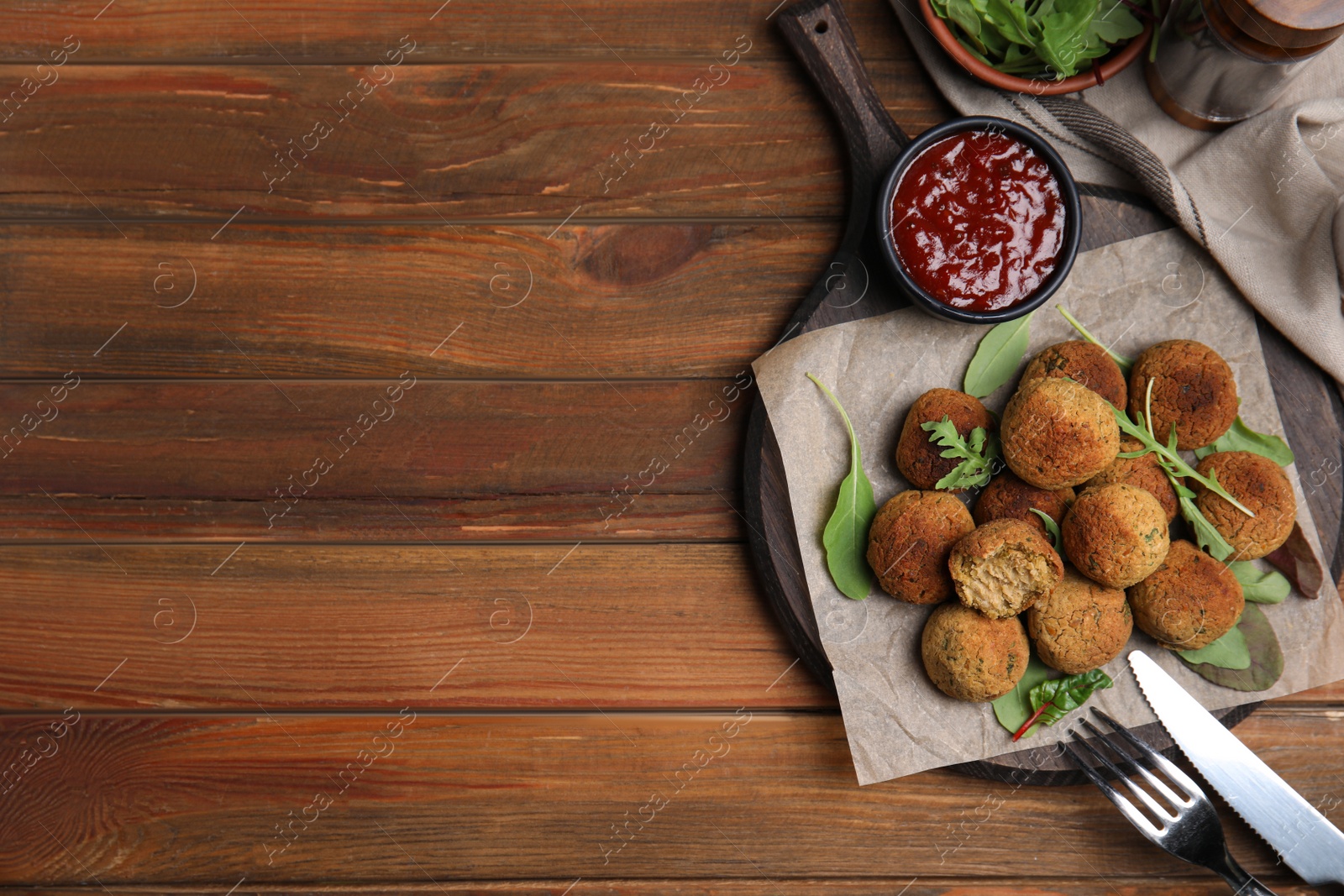 Photo of Delicious falafel balls with herbs and sauce served on wooden table, flat lay. Space for text