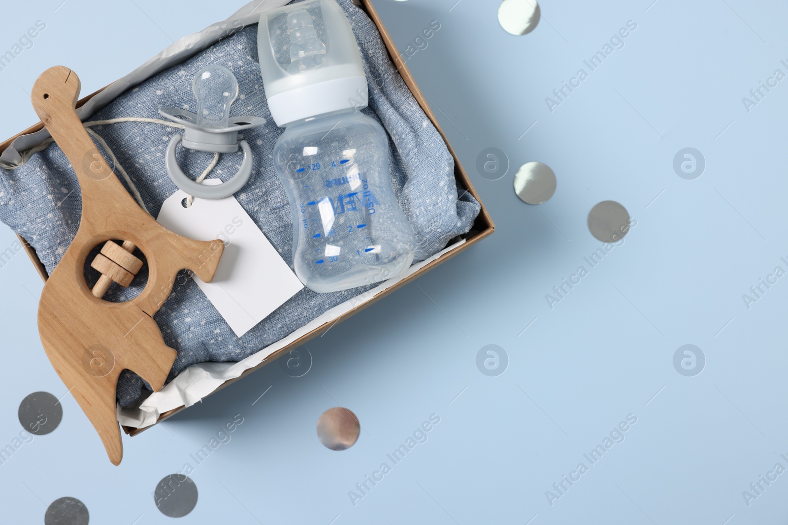 Photo of Different baby accessories with blank card in box and confetti on light blue background, top view. Space for text