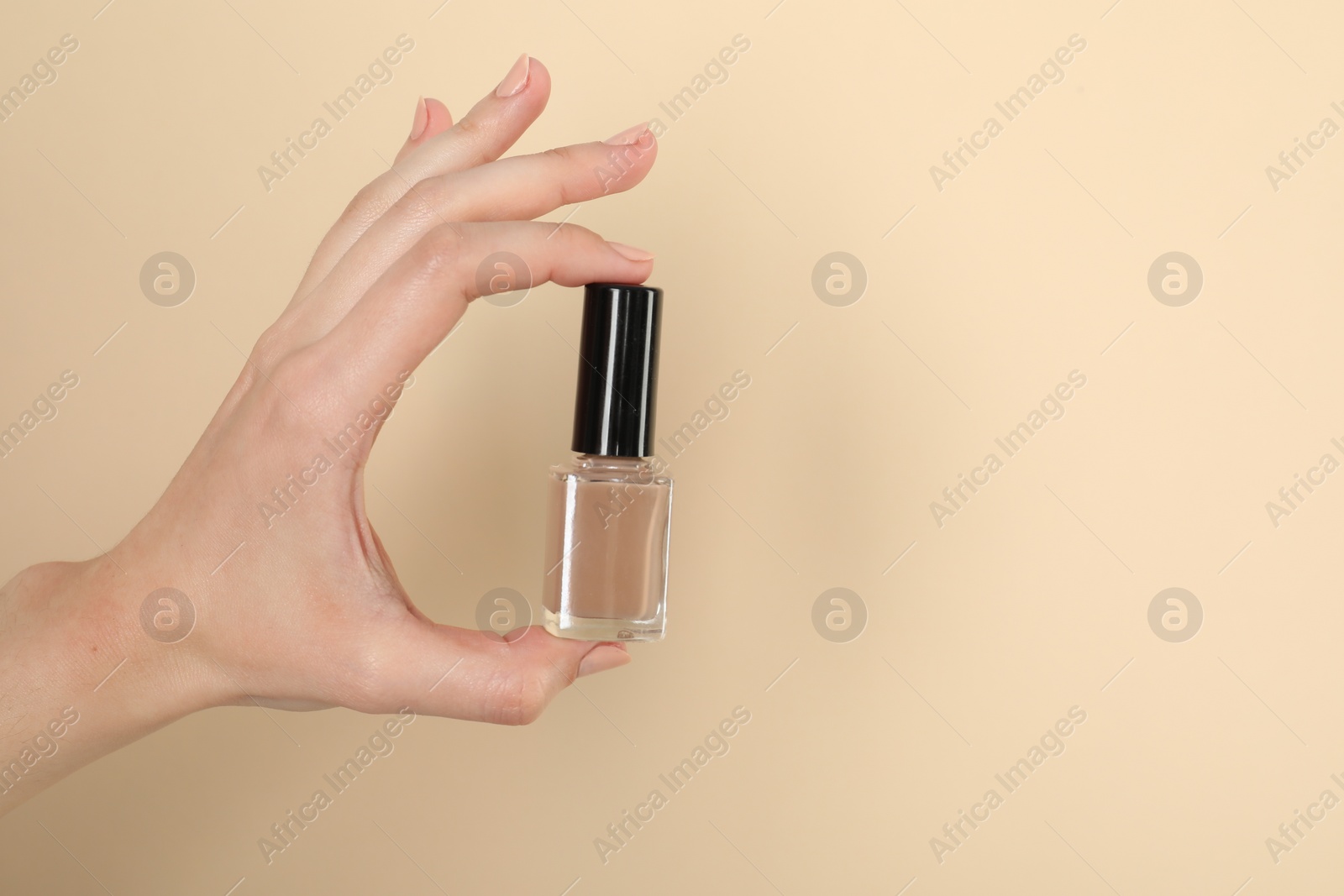 Photo of Woman holding nail polish on beige background, closeup. Space for text